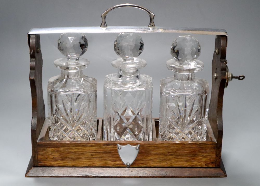 An oak three bottle tantalus, with key, decanters not matching, width 35cm